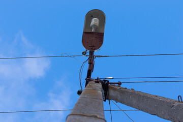 Obraz premium Old concrete lighting pole with a single lamp and wires against the sky. View from the bottom.