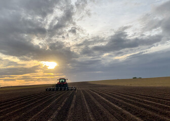 Naklejka premium A red tractor farming as the sun sets