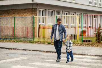 A father and son crossing a crosswalk while holding hands.