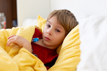 Sick child, toddler boy lying in bed with a fever, having breakfast, resting at home