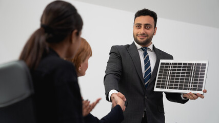 A confident businessman presents a solar panel to colleagues, demonstrating renewable energy...