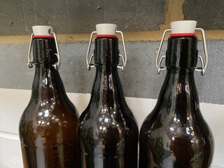3 flagon bottle in a row, swing top brown bottles for beer or ale grey brick background