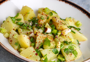 Potato salad with green onion on white plate over wooden background with copy space. Top view.