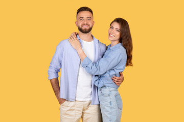 Happy loving couple embracing, smiling on yellow background