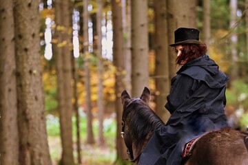 Schwarze Frau. Dunkel gekleidete Reiterin auf schwarzem Pferd im finsterem Wald