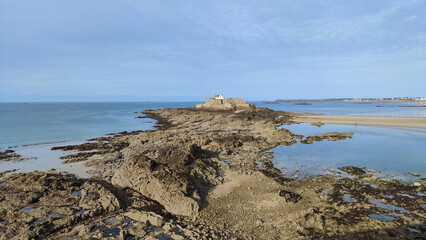 Fototapeta na wymiar Photograph of coastal beach landscape with rock formations with the National Fort in Saint Malo