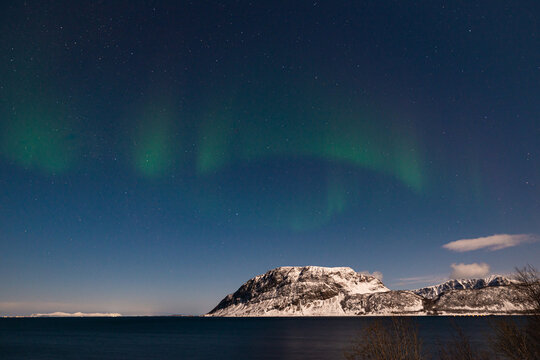 Green colored northern lights dance in the sky above snowy mountains on the Lofoten Islands in Norway