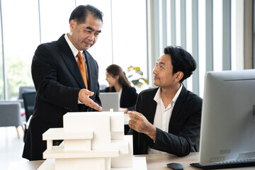 Senior businessman explaining a structural model to a junior colleague with a laptop in a modern...