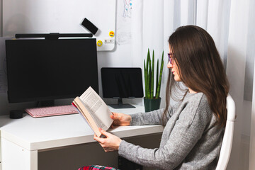 Close-up of young female sitting on home office reading a book