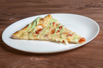 close-up of one piece of pizza on a white plate. Wooden table