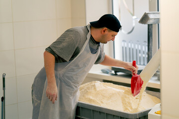 outline of a baker leveling the flour that is pouring in a container in professional kitchen