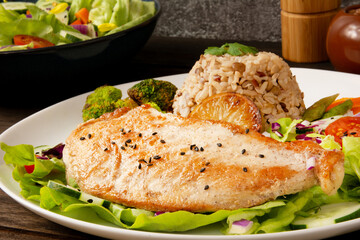 Grilled chicken in a plate with salad and rice sprinkled with sesame seeds front view