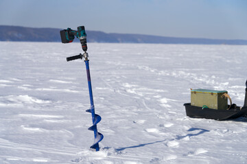 Panoramic view of frozen river under snow with fishermen's attributes (ice drill and box with catch...