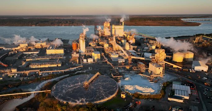 Sunrise view of a paper mill in Brunswick, Georgia, with visible effluent ponds and industrial activity, suggesting environmental concerns like air and water pollution.