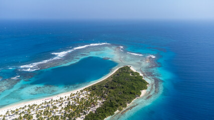 View of a small white sandy cay surrounded by a barrier reef and a deep blue sea