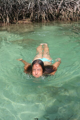 Girl emerging from under the turquoise water of the sea with a mangrove behind her