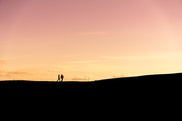 Unknown couple hiking in silhouette at sunset