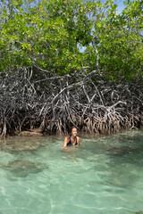 Girl emerging from the turquoise water of the sea with a mangrove behind her