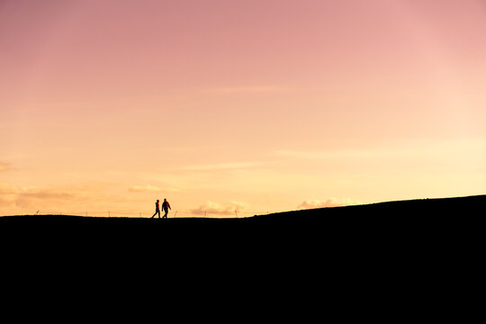 Unknown couple hiking in silhouette at sunset