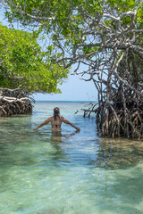 Woman in clear turquoise water between two mangroves with the sea in the background