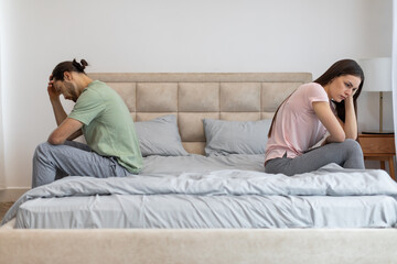 Upset couple sitting apart on bed, facing away