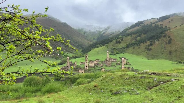 View of the medieval Targim tower complex in the Caucasus mountains surrounded by greenery. The Caucasus Mountains on a cloudy day in Ingushetia. Russia, 4K.