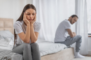 Upset woman on bed with man in background, tension visible