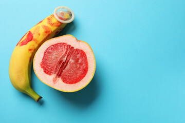 Half of grapefruit, banana with condom and red lipstick marks on light blue background, flat lay...