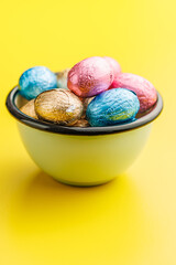 Easter chocolate eggs wrapped in aluminium foil in bowl on yellow background.