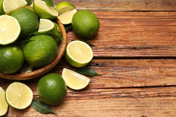 Fresh limes and green leaves with water drops on wooden table. Space for text