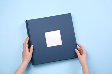 Woman with photo album at light blue background, top view
