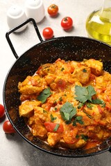 Delicious chicken curry in frying pan and tomatoes on light grey table