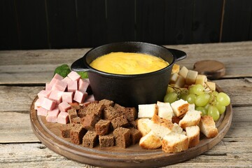 Fondue pot with melted cheese and different products on wooden table