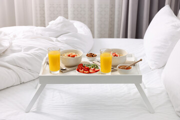 Tasty breakfast served in bed. Oatmeal, juice, fruits, almonds and honey on tray