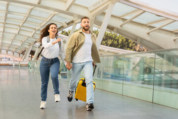 Young couple in rush running with yellow suitcase at the airport