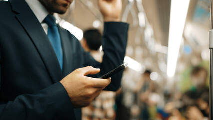 Closeup of business man hands looking phone while standing at train surrounded by people. Caucasian...