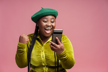 Stylish overjoyed African American woman holding mobile phone win money celebration success...