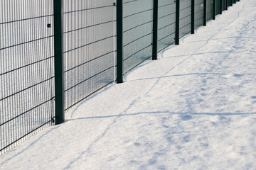 Green metal fence in winter in the snow.