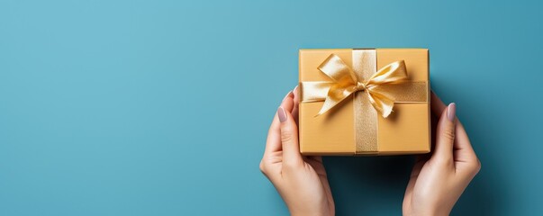 Woman holding gift box with ribbon bow on pastel blue background. Present for birthday, Valentine's, Women's and Father's day, Christmas.  Flat lay, top view with copy space