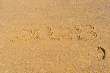 Fototapeta na wymiar 2028 written in the sand on the beach with a single footprint - Happy New Year