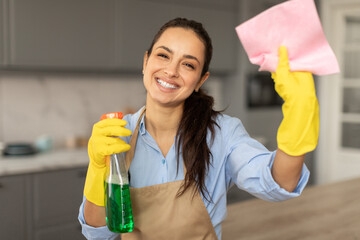 Cheerful woman cleaning with spray and rag