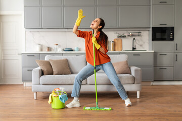 Joyful woman dancing with mop in modern living room