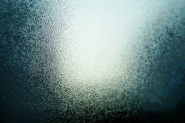 Abstraktes Motiv mit Eisbedeckter Glasscheibe vor blauem Himmel mit weißer Sonne bei Kälte, Frost und Sonne am Morgen im Winter