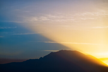 Sunrise in mountains, shadow in sky from mountains and sunlight rays glowing, nature landscape background