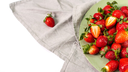 Red strawberries on a light green plate with gray linen napkins on a white background.