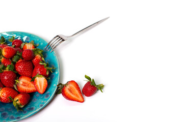 Red fresh strawberries in a blue ceramic plate on a white background with a fork. close-up.