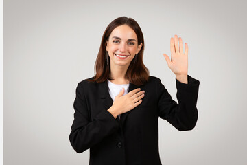 Pleasant businesswoman with a sincere smile raises her right hand to take an oath or pledge