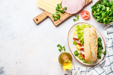 Ciabatta sandwich with lettuce, cheese, tomatoes and ham on white table.