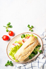 Ciabatta sandwich with lettuce, cheese, tomatoes and ham on white table.