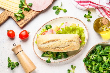 Fototapeta na wymiar Ciabatta sandwich with lettuce, cheese, tomatoes and ham on white table.